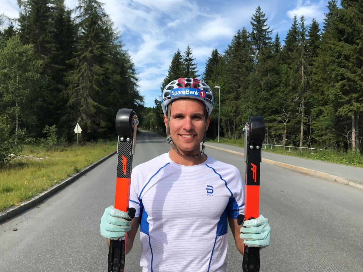 Didrik Tønseth smiling while holding a pair of FF rollerskis during a summer training session on the road.