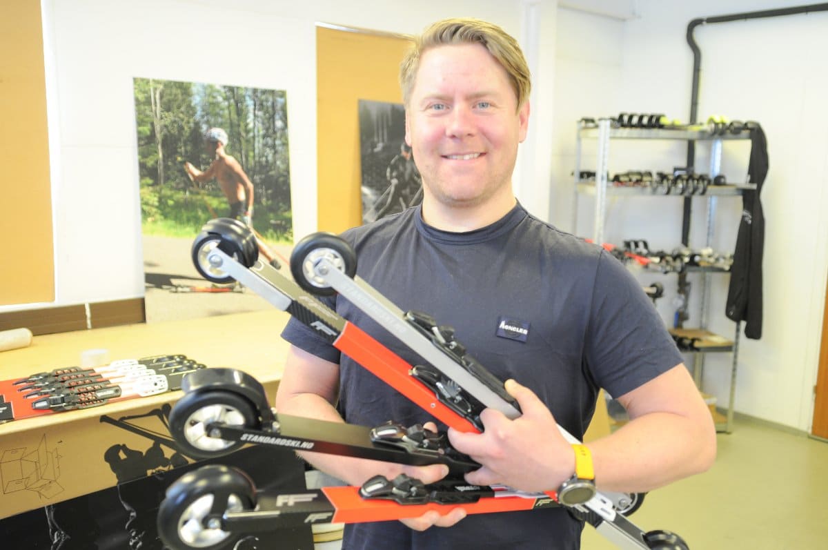 Henrik CEO of FF Rollerskis smiling while holding several pairs of high-performance rollerskis in his workshop.